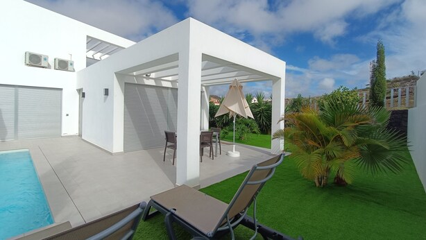 Un patio moderno al aire libre con piscina, una zona de estar cubierta y césped artificial.
