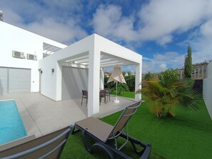 Een modern terras buiten met een zwembad, een overdekte zithoek en kunstmatig groen gazon.