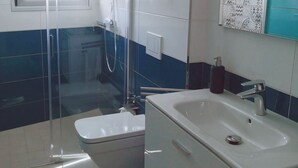 Un baño con ducha de vidrio, un lavamanos blanco y un espejo con azulejos decorativos.