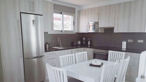 Una cocina moderna con armarios blancos, electrodomésticos de acero inoxidable y un comedor con sillas blancas.