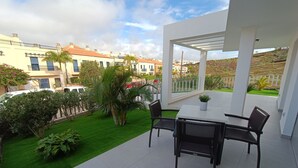 Un patio con una mesa y sillas, rodeado de un césped cuidado y plantas en macetas.