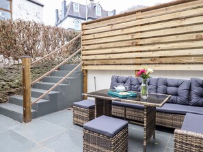 A patio area with wicker furniture, a table with a tray, and a vase with flowers.