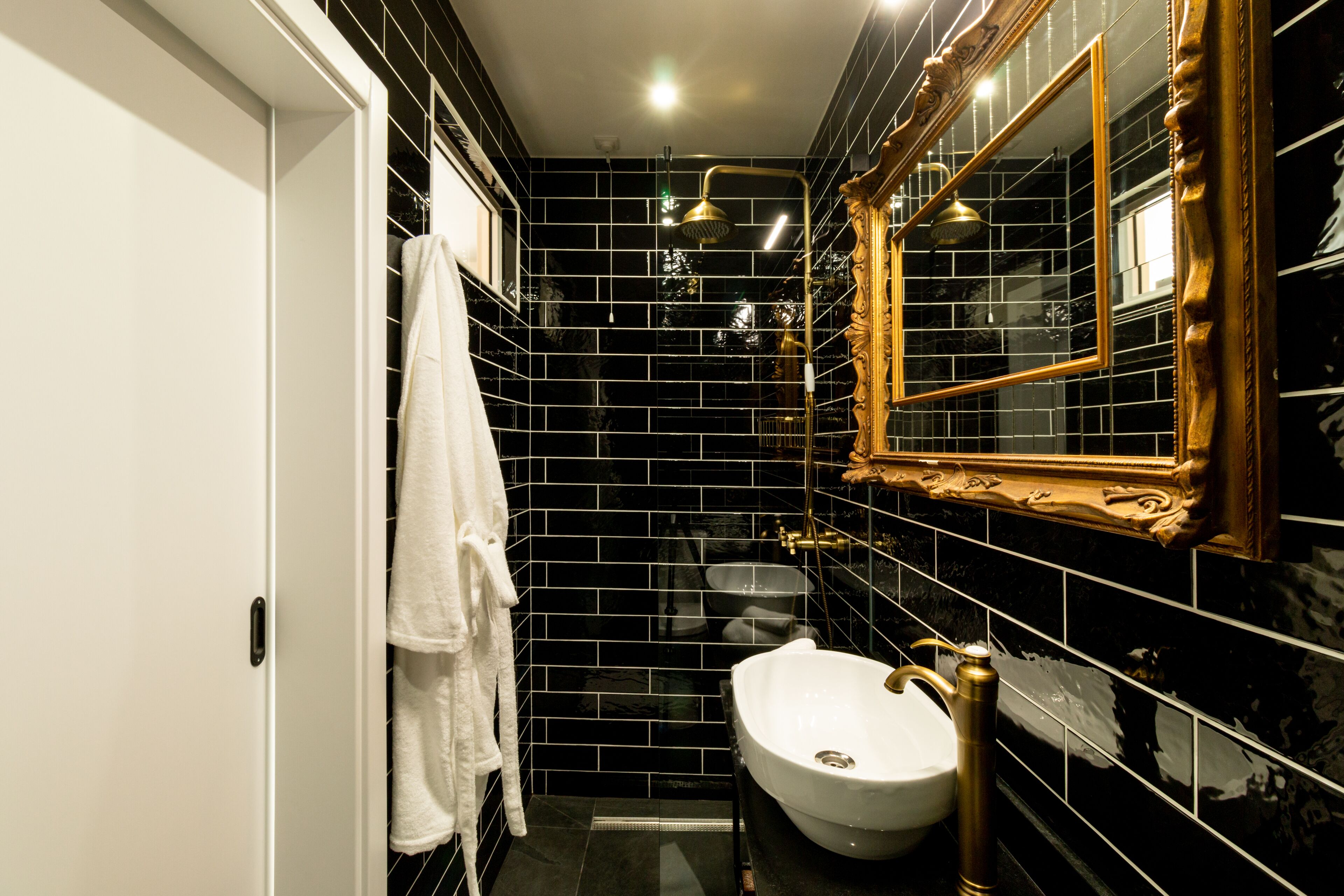 A bathroom with black tiled walls, a white sink, and a gold-framed mirror.