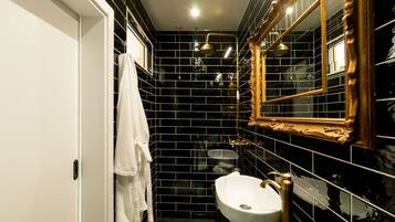 A bathroom with black tiled walls, a white sink, and a gold-framed mirror.