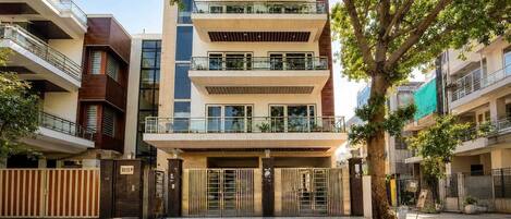 A multi-story residential building with a gated entrance, balconies, and a tree in the foreground.