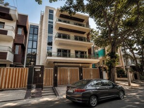 A multi-story residential building with a gated entrance, a parked car, and trees in the background. - Lime Tree Luxury 3Bhk Serviced Apartment (Gurugram)