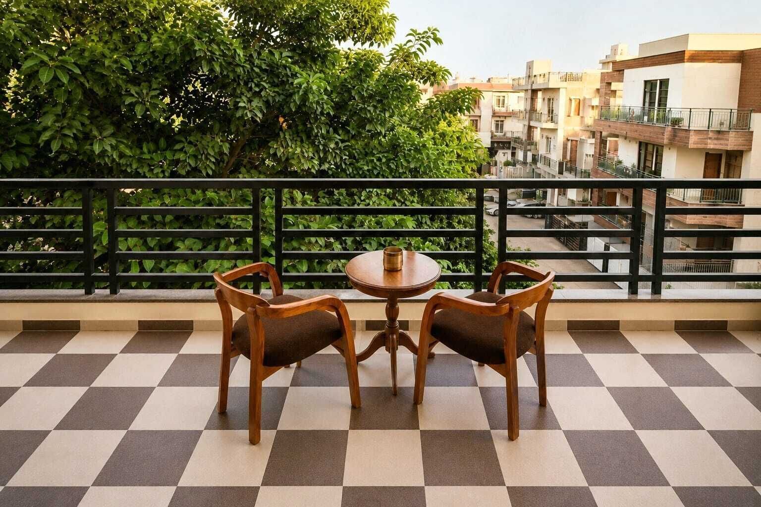 Ein Balkon mit Schachbrettboden, zwei Holzstühle, ein kleiner runder Tisch und Blick auf Häuser und Grünflächen.