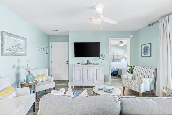 A living room with a ceiling fan, a television, a white cabinet, and striped armchairs.
