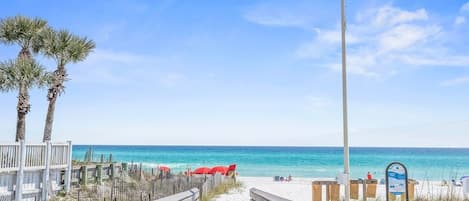 A wooden boardwalk leading to a sandy beach with palm trees and a clear blue sky.