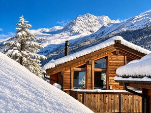 Una baita di legno dal tetto imbiancato dalla neve, ampie finestre e vista sulle montagne innevate.