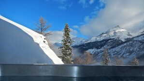 Panorama di una catena montuosa innevata, cielo sereno e specchio d'acqua in primo piano.