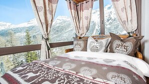 Una camera da letto con vista sulle montagne, con un letto e biancheria a motivi e cuscini a forma di cuore.