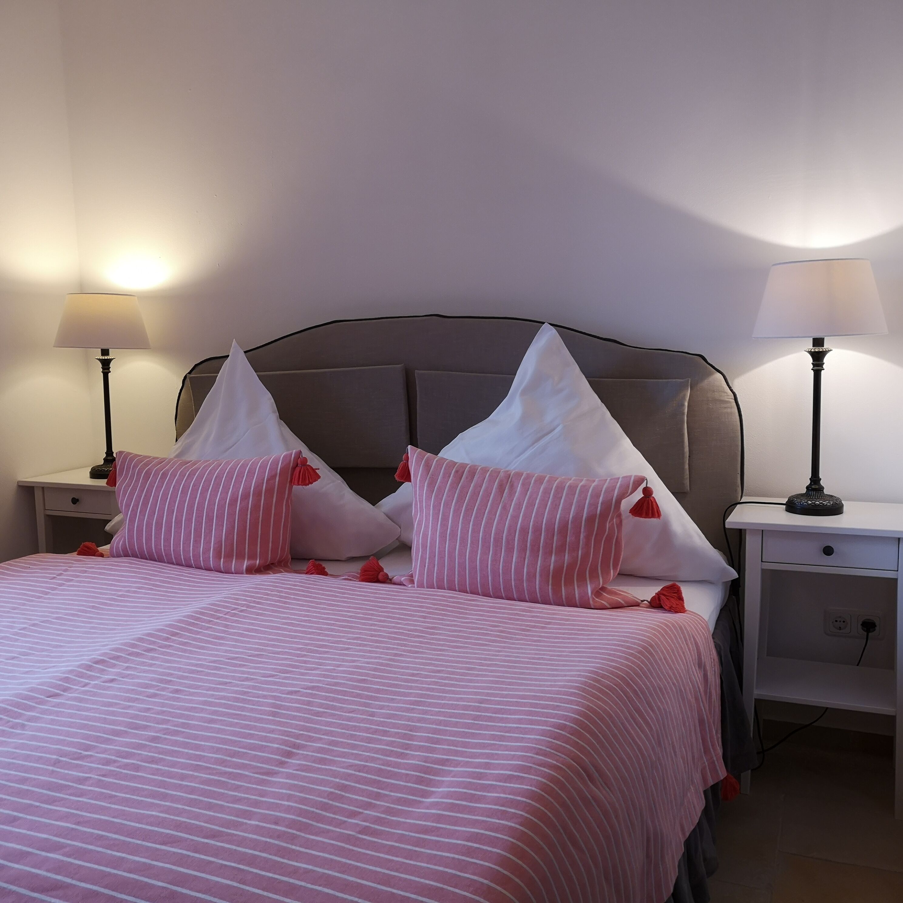 A neatly made bed with striped bedding, two bedside tables with lamps, and a headboard.