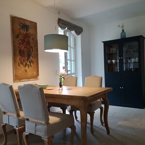 A dining area with a wooden table, four chairs, a vase with flowers, a painting on the wall, and a cabinet with glass doors.