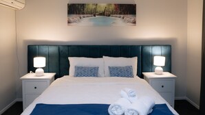 A neatly made bed with a blue accent, two bedside lamps, and a painting of a waterfall above it.