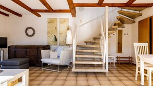 Un salon comprenant un canapé, un fauteuil blanc, une table, un escalier et un mur orné d’œuvres d’art abstraites.