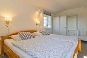 A double bed with floral bedding, two wall-mounted lamps, a window with blinds, and a white wardrobe.
