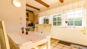 Une cuisine avec un coin repas, une fenêtre avec des rideaux et une vue sur la verdure à l’ext érieur.