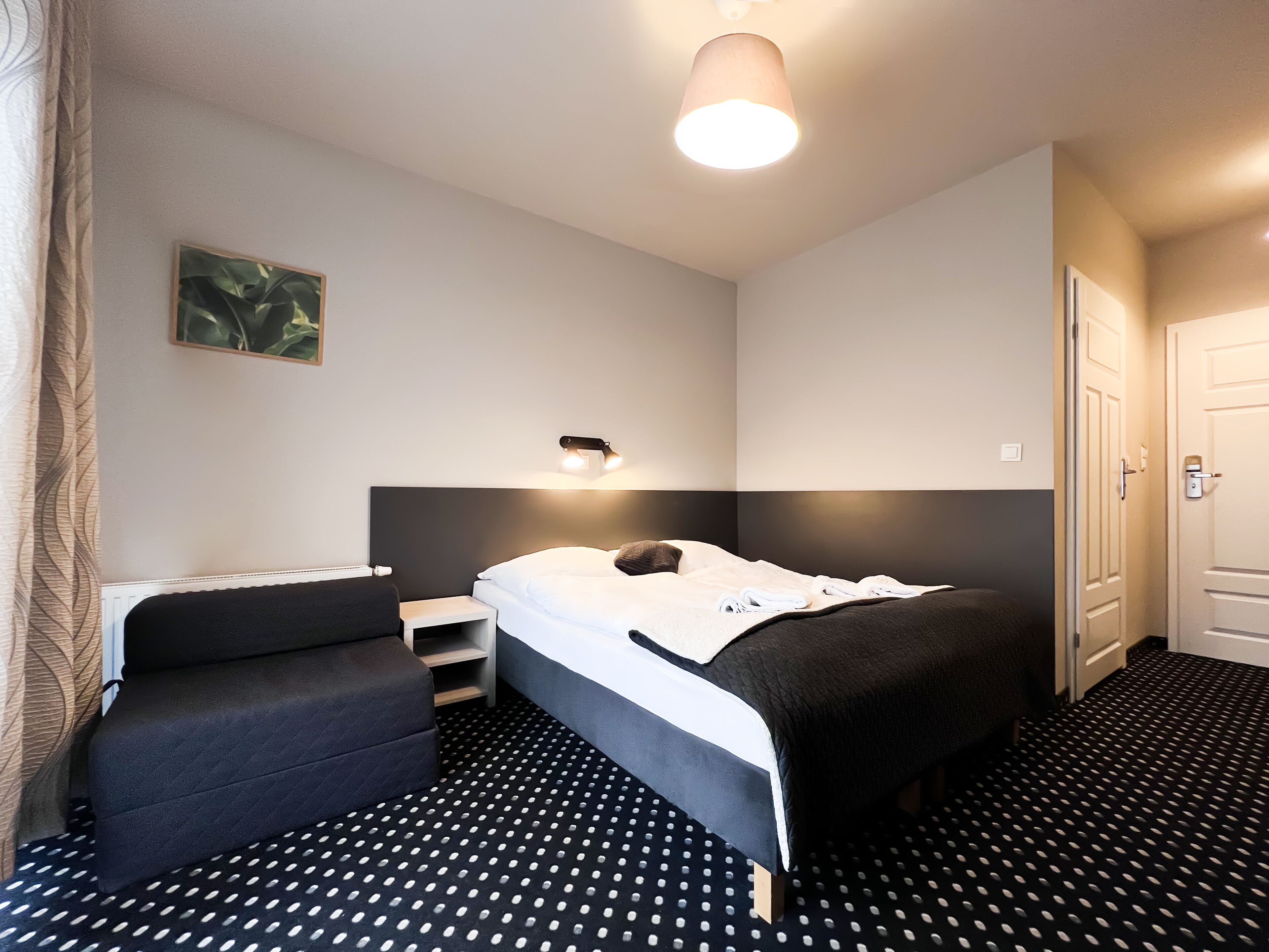A modern hotel room with a bed, bedside table, and a small seating area.