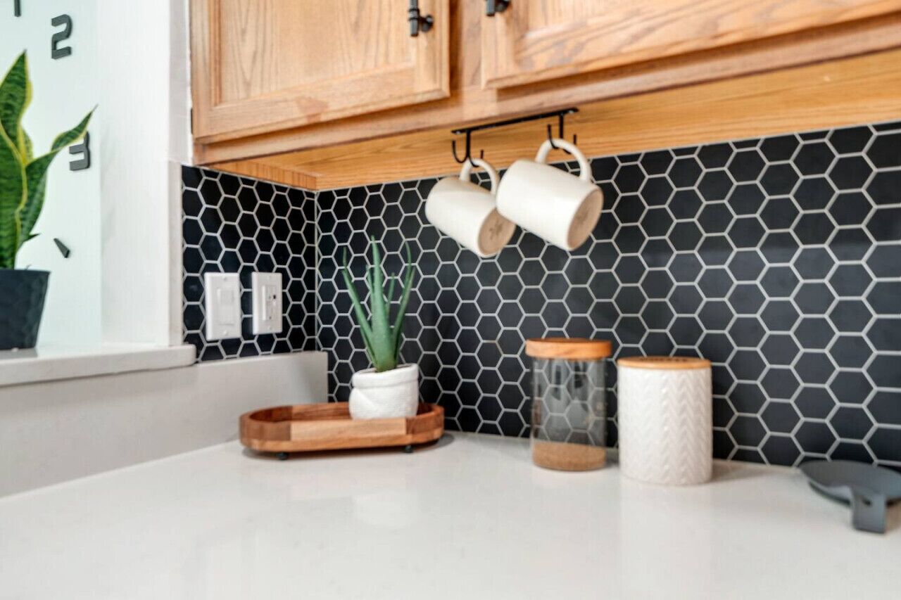 A kitchen with wooden cabinets, a black and white hexagonal backsplash, and a white countertop.
