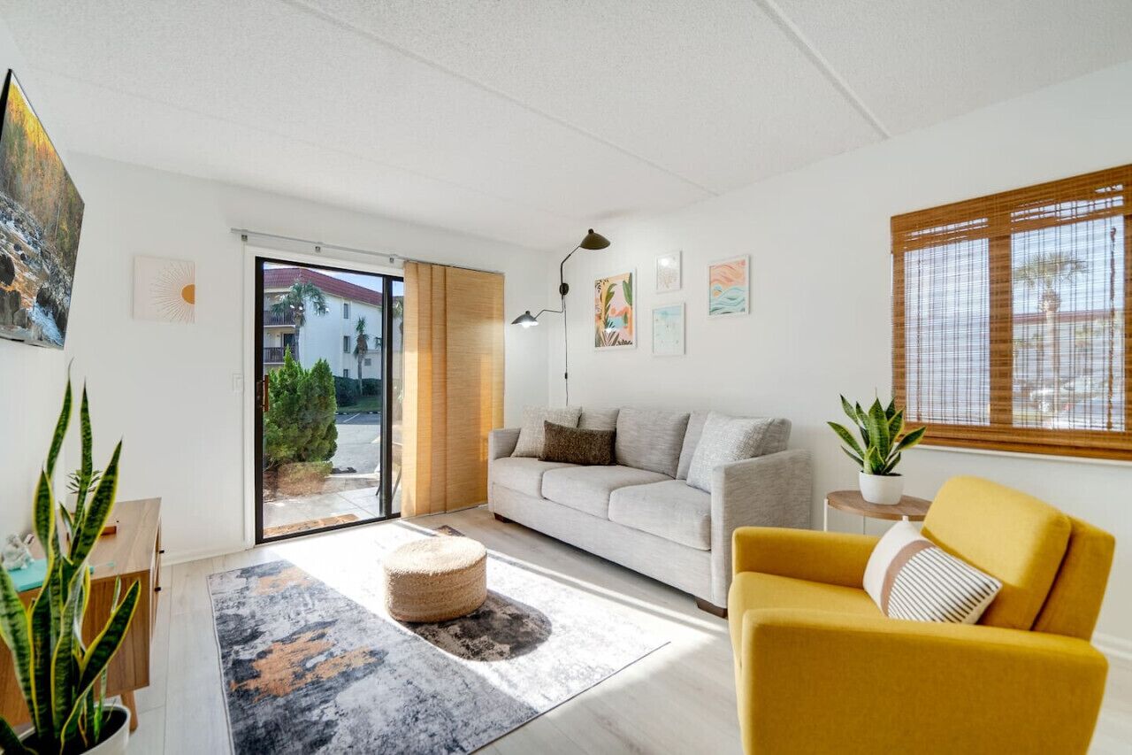 Ein modernes Wohnzimmer mit einer Couch, einem gelben Sessel, einem Couchtisch und einem großen Fenster mit Ausblick.