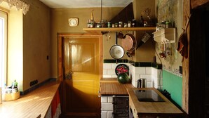 Une cuisine avec des meubles de rangement en bois, un luminaire vert suspendu, une horloge et divers ustensiles de cuisine.