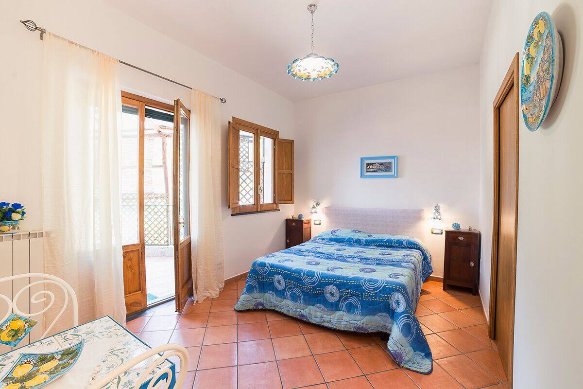 A bedroom with a bed, two bedside tables, a window, a door, and a ceiling light.