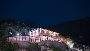 Un edificio a due piani con un balcone, situato su una collina con montagne sullo sfondo.