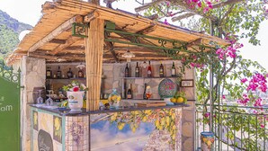 Un’area bar con un tetto in legno rustico, una parete piastrellata decorata con un murale raffigurante un panorama urbano e una selezione di bottiglie e bicchieri.