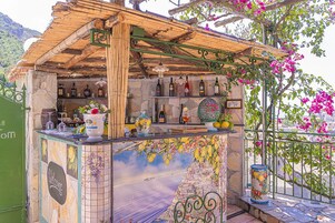 Un área de bar con techo de madera rústica, pared de azulejos con un mural de paisaje urbano y una variedad de botellas y vasos.