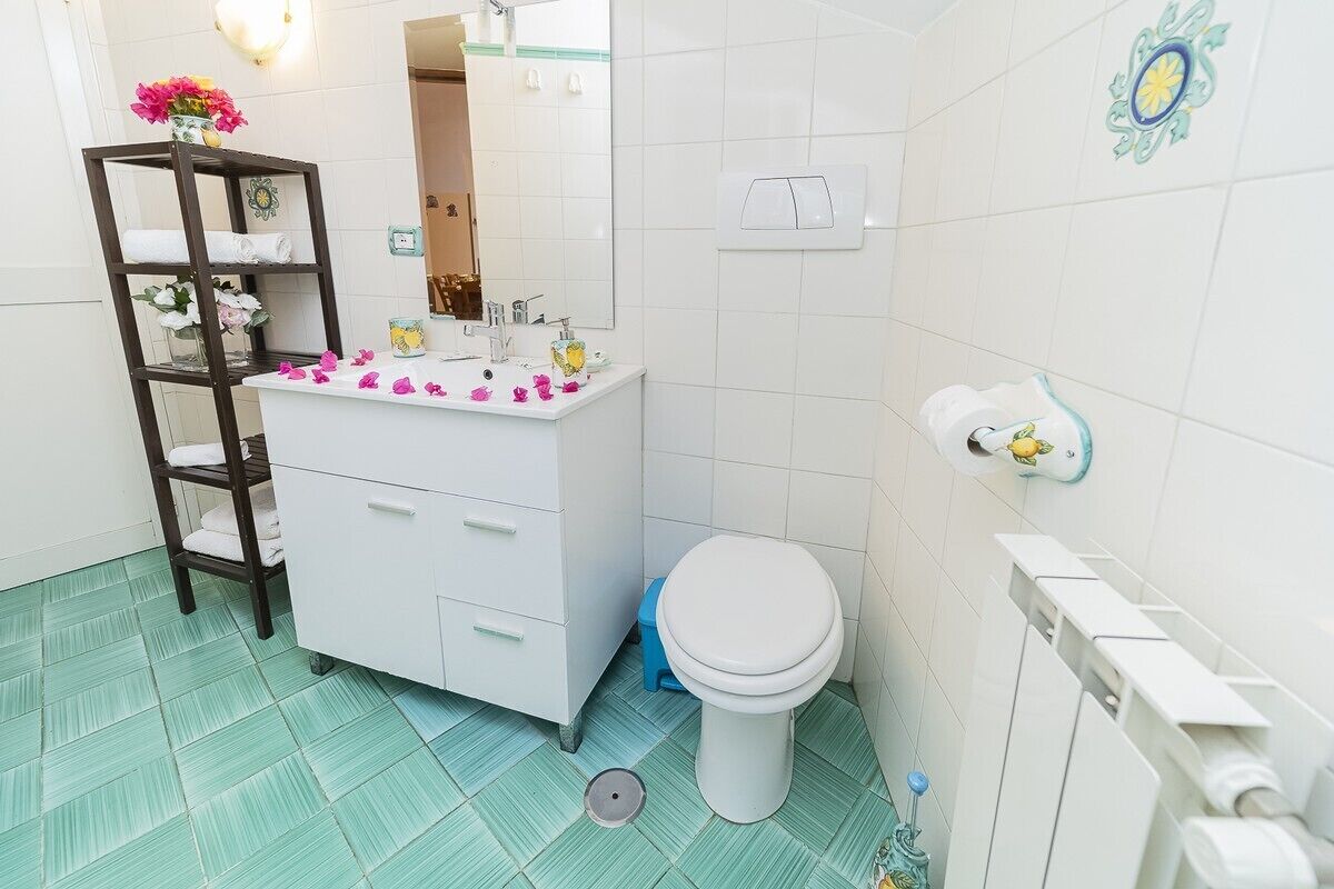 A bathroom with a white sink, a toilet, a shelf with towels, and a decorative mirror.