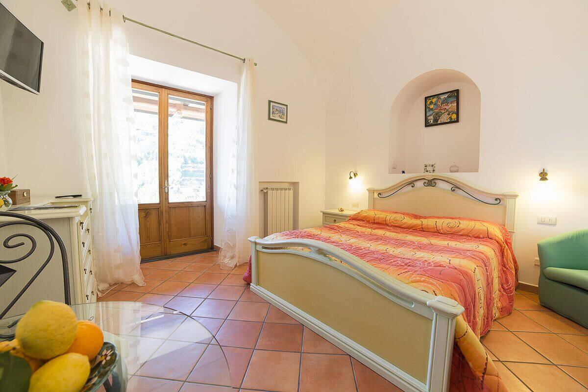 A bedroom with a bed, a window with curtains, a radiator, and a green chair.