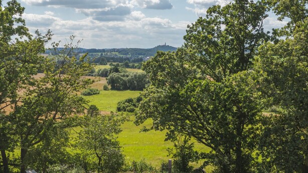 A large white tent with a conical roof, surrounded by a grassy area with trees and a distant view of hills. - Glamping in Stunning Bell Tent in Bohemia (Čmelíny)