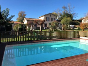 Une piscine dotée d’une terrasse en bois, entourée d’une clôture en bois et d’une pelouse.