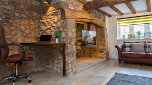 A stone-walled room with a wooden ceiling, a desk with a laptop, a TV, a leather chair, and a sofa with cushions. - Stunning 4 Bed Sleeps 8 Cottage Parking (Gloucester)