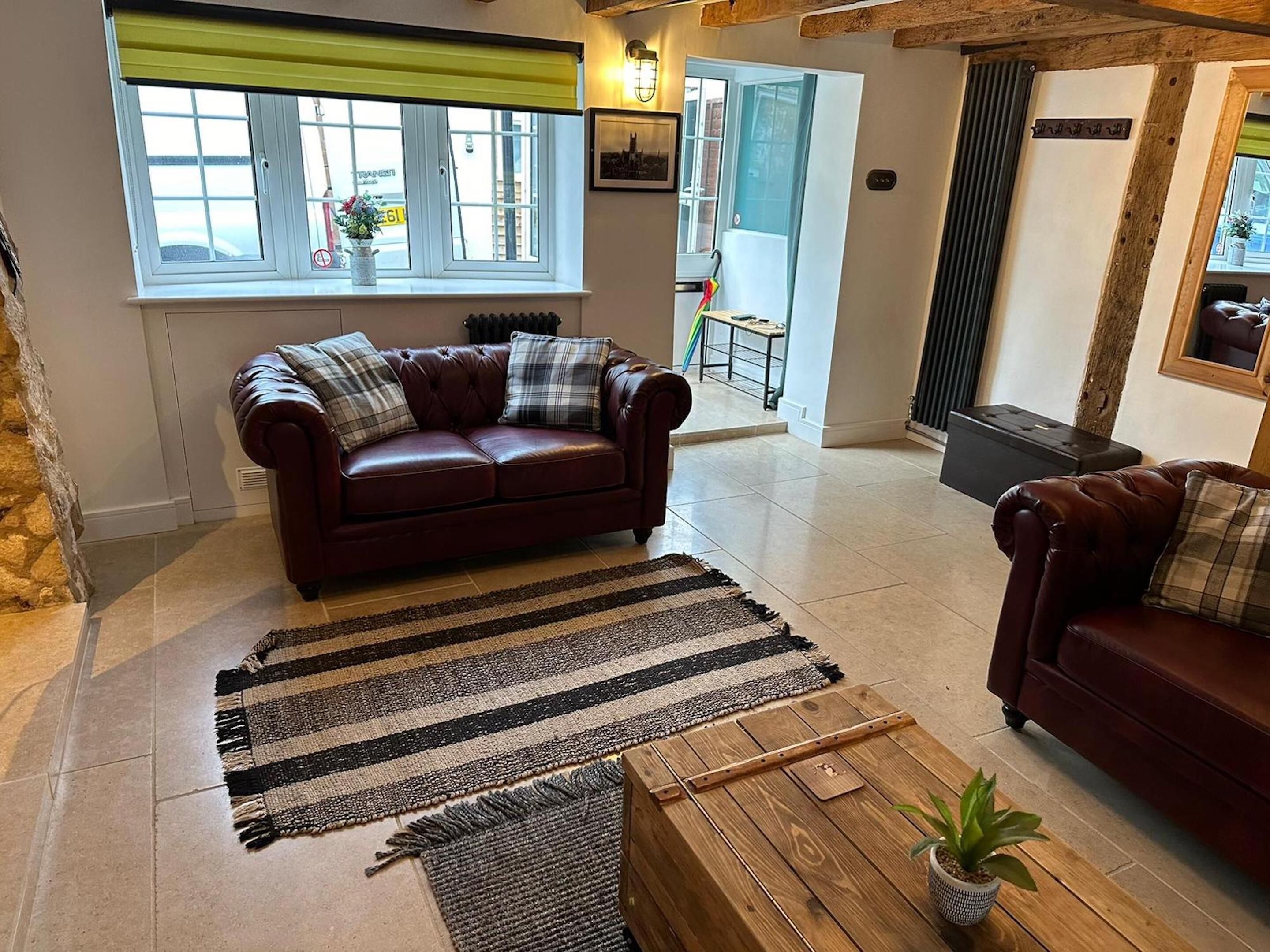 Una sala de estar acogedora con un sofá de cuero marrón, un tapete a rayas y una mesa de centro de madera con una planta en maceta.