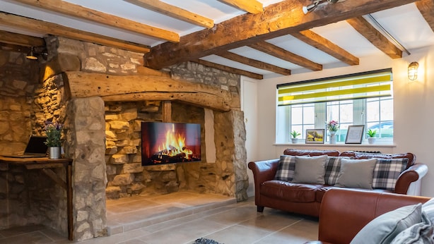 A cozy living room with a stone fireplace, a leather sofa, and a flat-screen TV mounted on the wall. - Stunning 4 Bed Sleeps 8 Cottage Parking (Gloucester)
