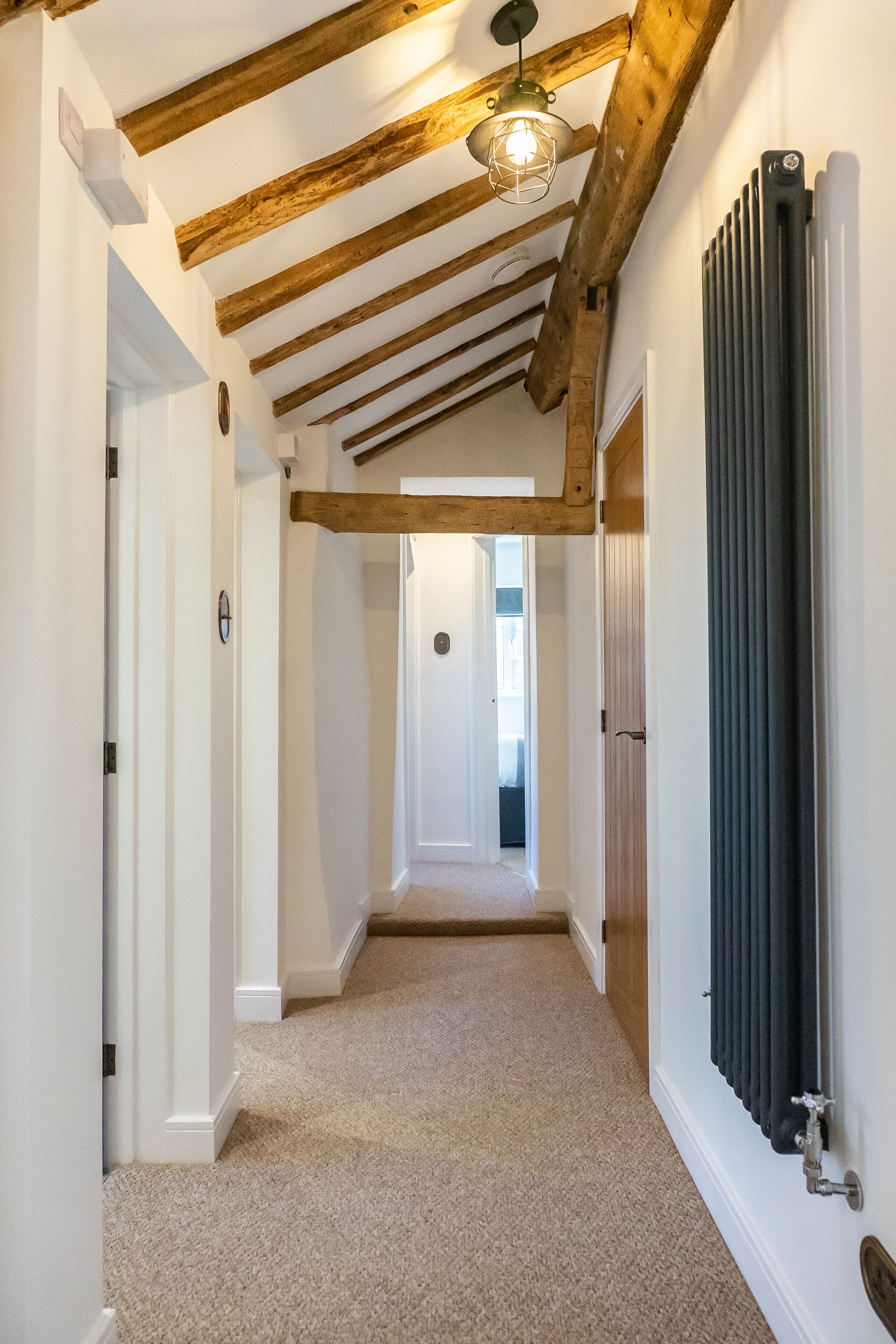 A hallway with exposed wooden beams, a radiator, and a carpeted floor.