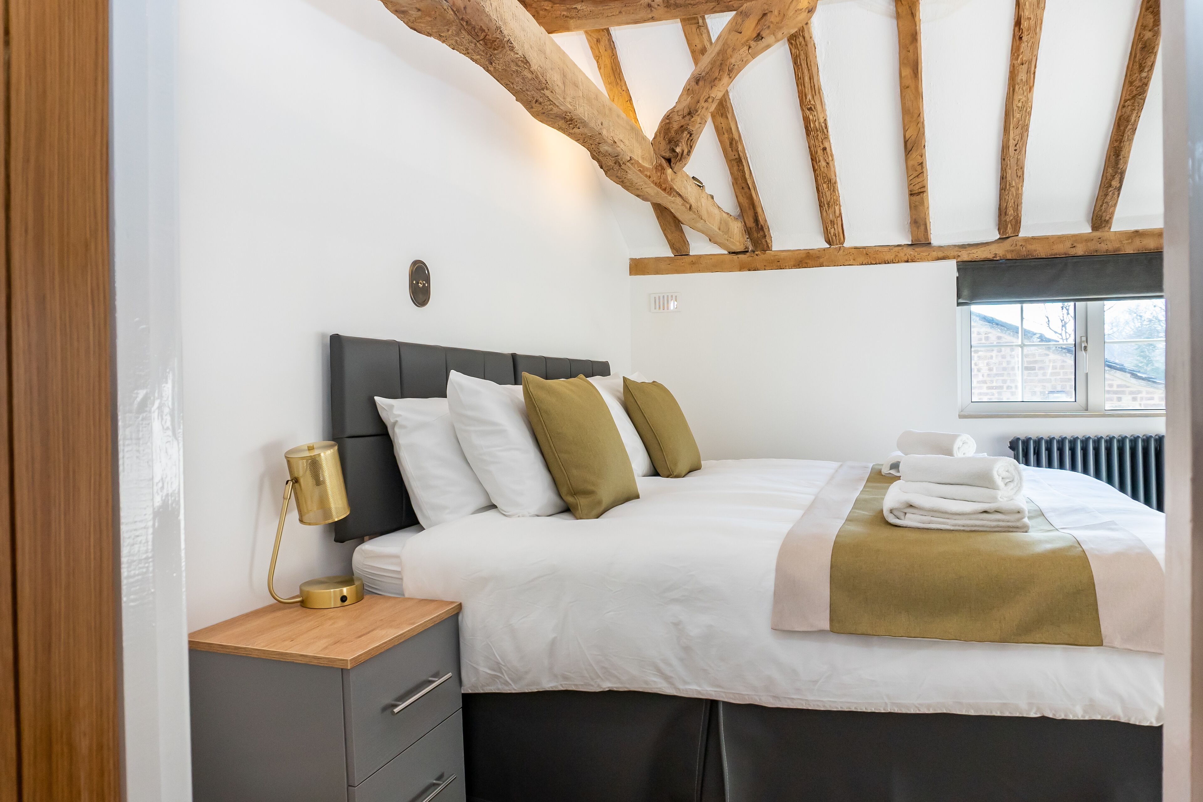 A neatly arranged bedroom with a bed, bedside table, lamp, and a window with a view of the outside.