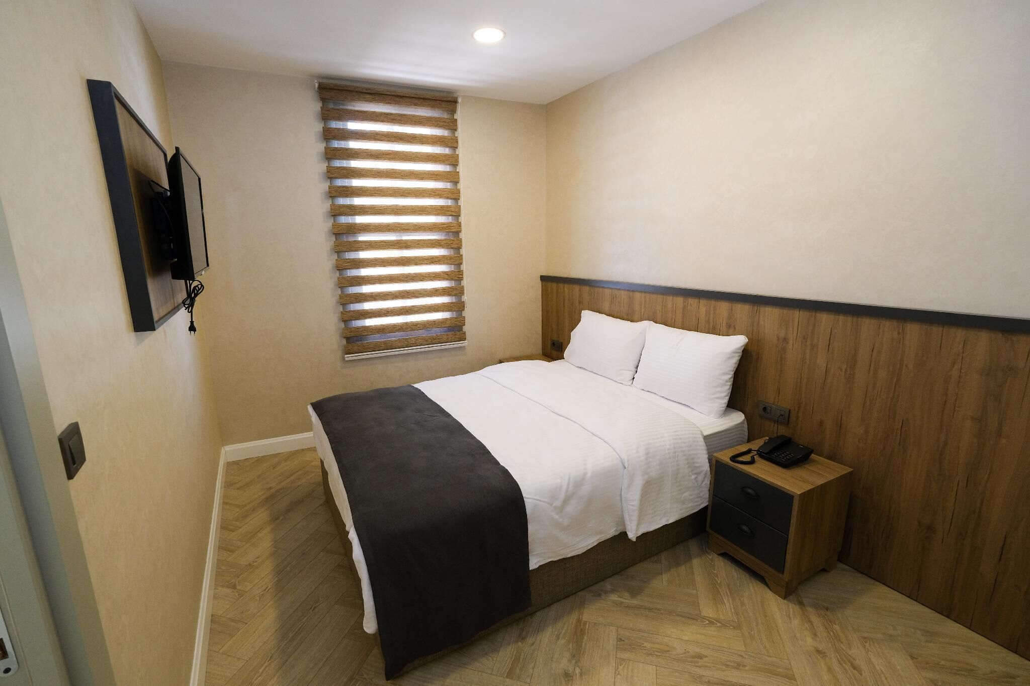 Un dormitorio con cama, mesita de noche y televisión montada en la pared.
