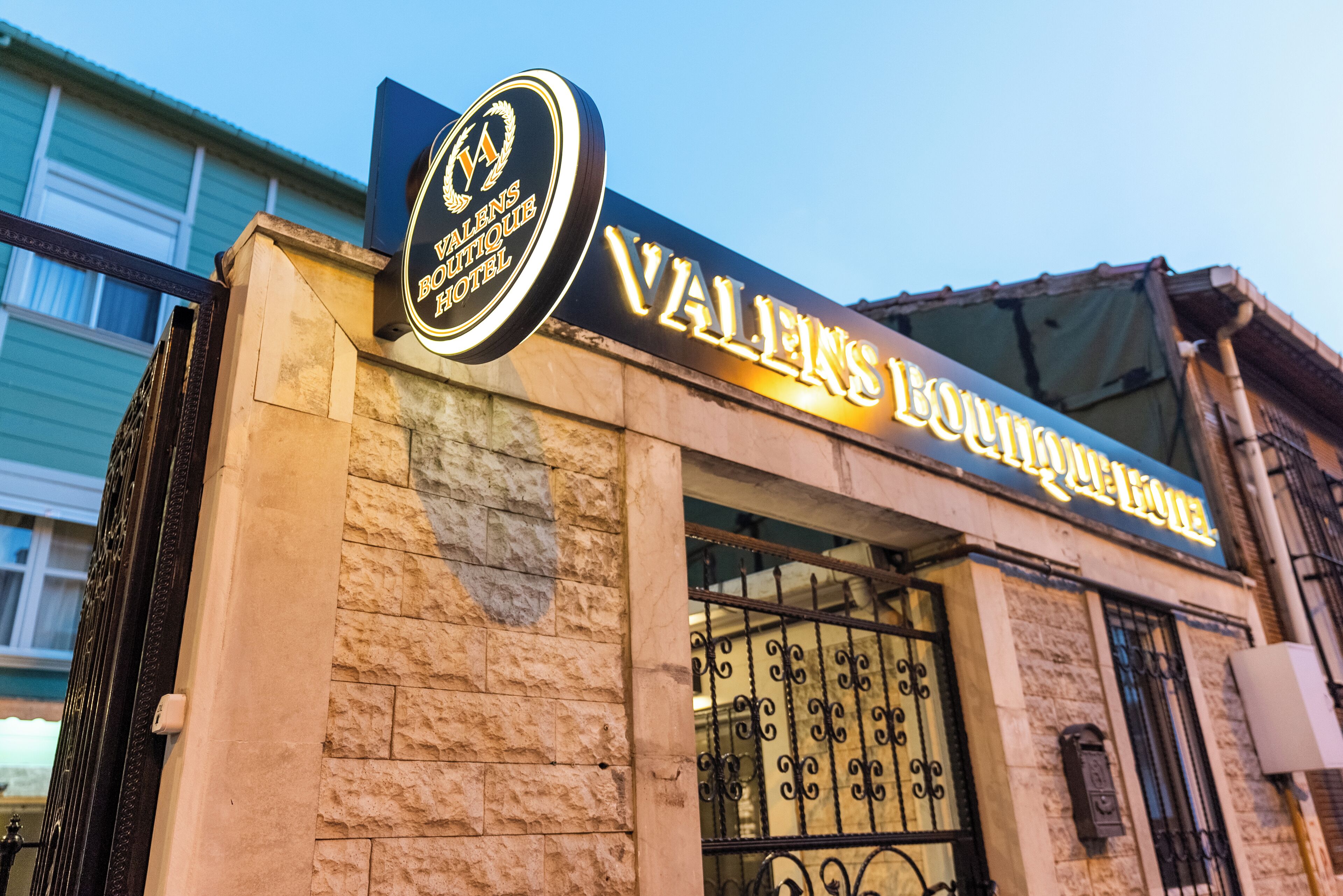 The exterior of the Valens Boutique Hotel with a prominent sign and a stone facade.