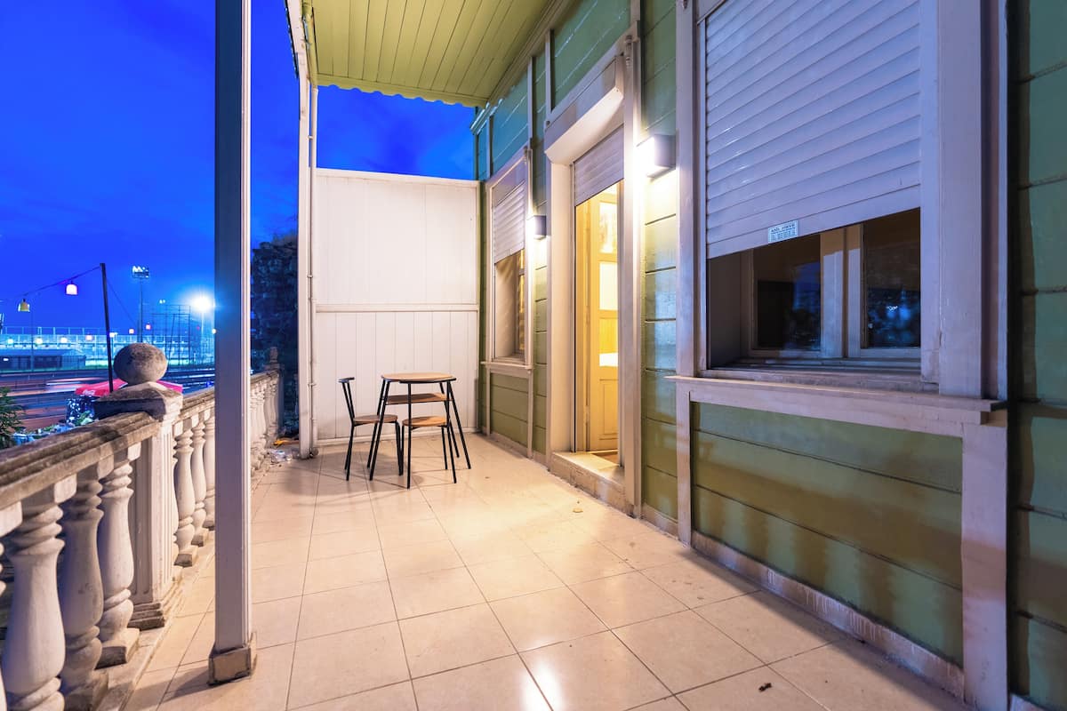 A balcony with a view of the city at dusk, a table and chairs, and a door leading to the interior.
