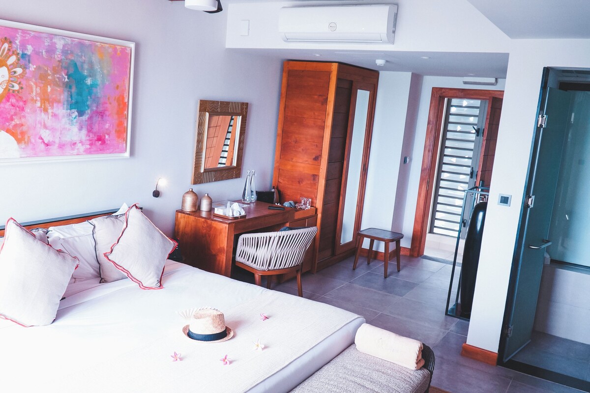 A hotel room with a bed, a desk, a chair, a mirror, and a door.