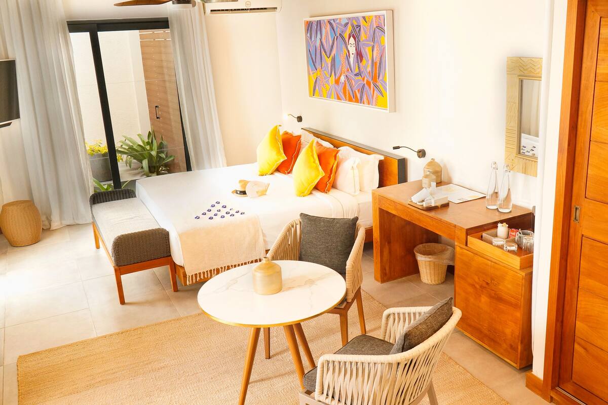 A hotel room with a bed, a desk, a chair, a small round table, and a TV.