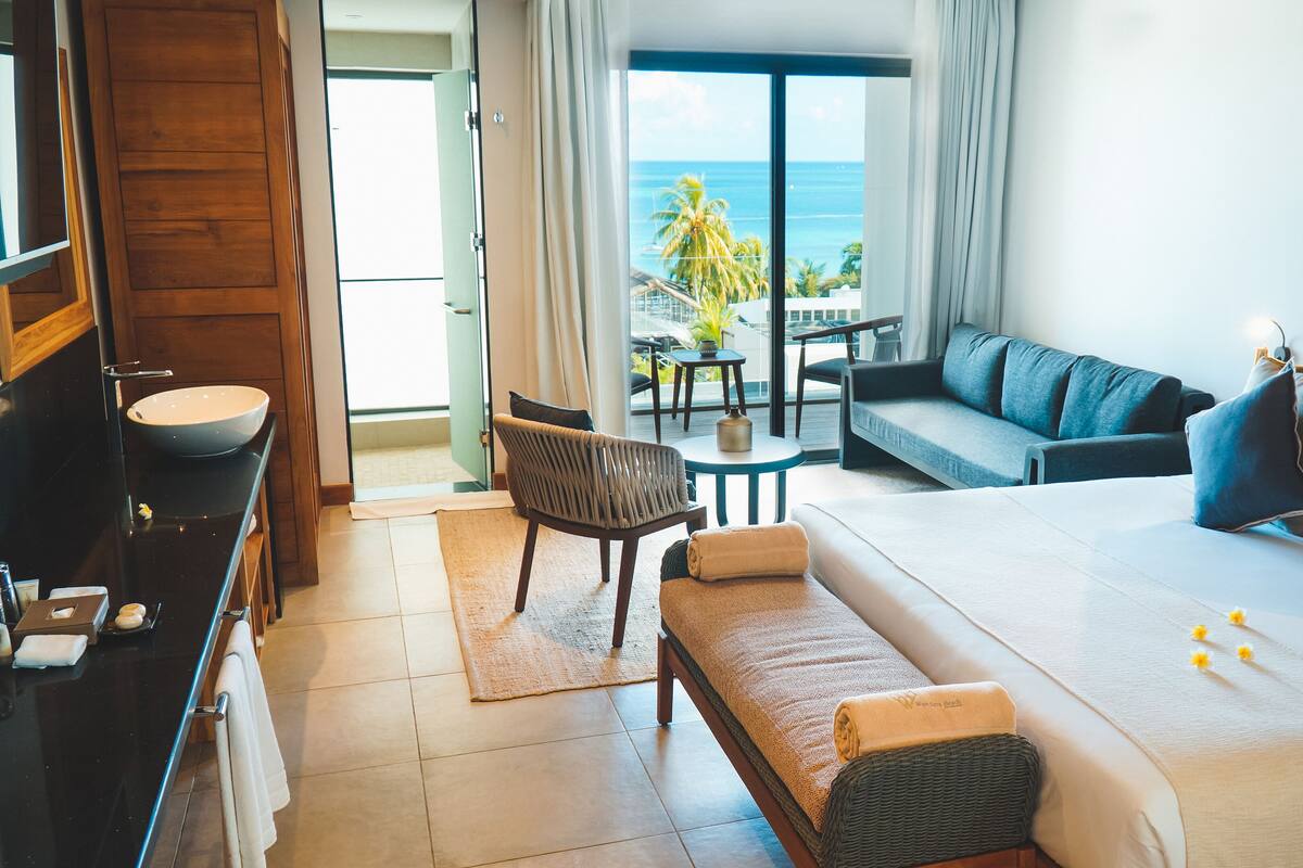 A hotel room with a bed, a sofa, a chair, a small table, and a view of the ocean.