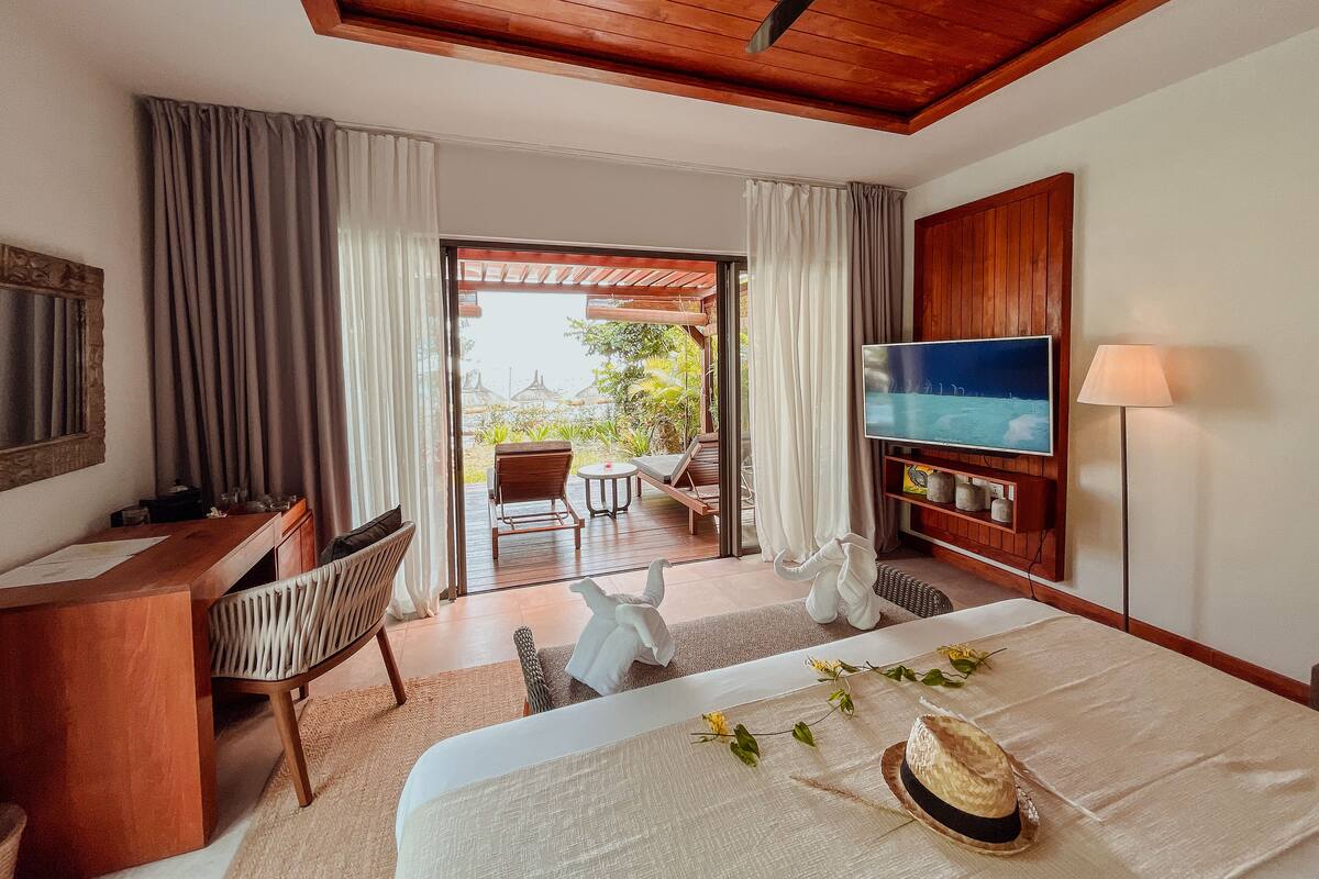 A hotel room with a wooden ceiling, a TV, a desk, a bed, and a view of the outdoors.