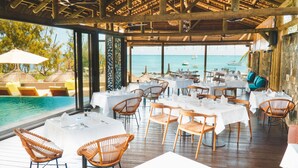 An outdoor dining area with tables and chairs, overlooking a pool and the sea. - Wonders Beach Boutique Hotel (Mont Choisy)