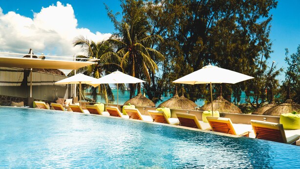 A poolside area with lounge chairs and umbrellas, surrounded by palm trees and a clear sky. - Wonders Beach Boutique Hotel (Mont Choisy)