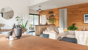 Un salon moderne avec un mur en bois, un miroir rond et un coin repas doté d’une table en bois.