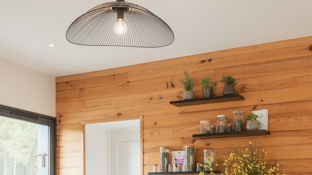 Une cuisine moderne avec un îlot central en bois, des tabourets de bar, un luminaire suspendu et une plante en pot.